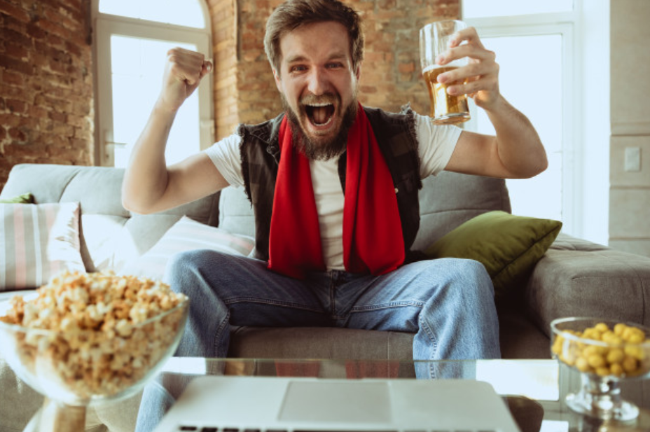 homem segurando um copo de cerveja se levantando do sofá para comemorar