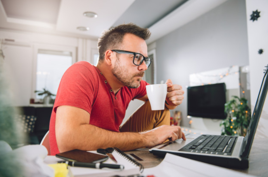 homem de óculos estudando estatísticas sentado em frente ao seu laptop e segurando uma xícara branca