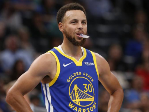 stephen curry usando uniforme roxo sorrindo e segurando um protetor bucal cinza com a boca