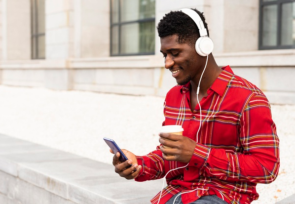 homem de fone branco e camisa listrada vermelha sorrindo enquanto olha para o celular