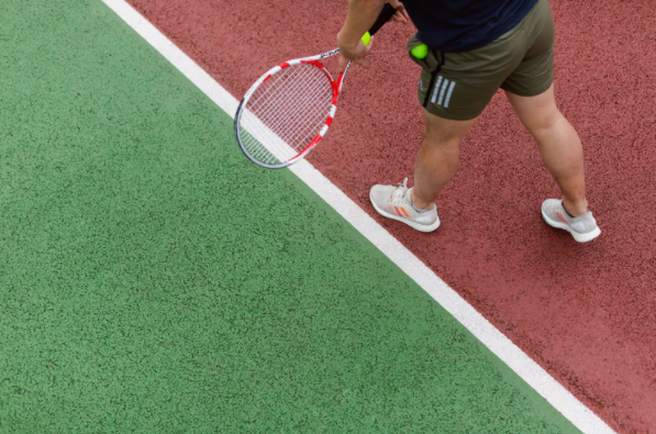 homem em quadra de tênis segurando raquete e bola de tênis enquanto guarda outra bola no bolso