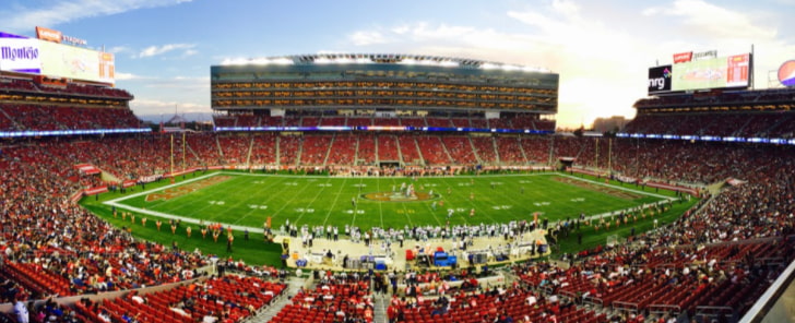 estádio de futebol americano durante uma partida durante o dia, lotado de torcedores.