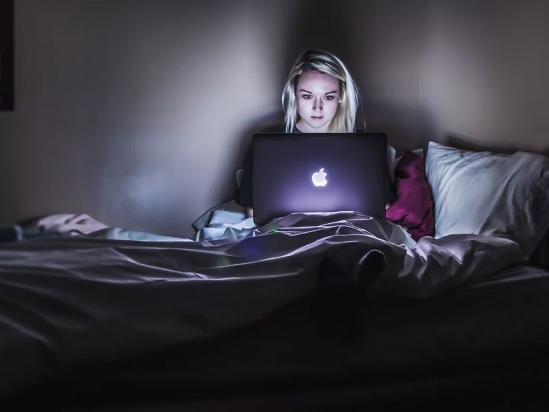 menina em uma cama, sentada em frente ao notebook com iluminação 